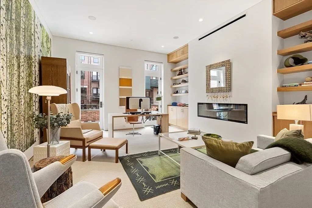 "Here's a charming little sitting area where you can relax and enjoy the warmth of the fireplace. I love how the natural light pours in through those big windows, and the greenery on the wall really brings the outdoors in."