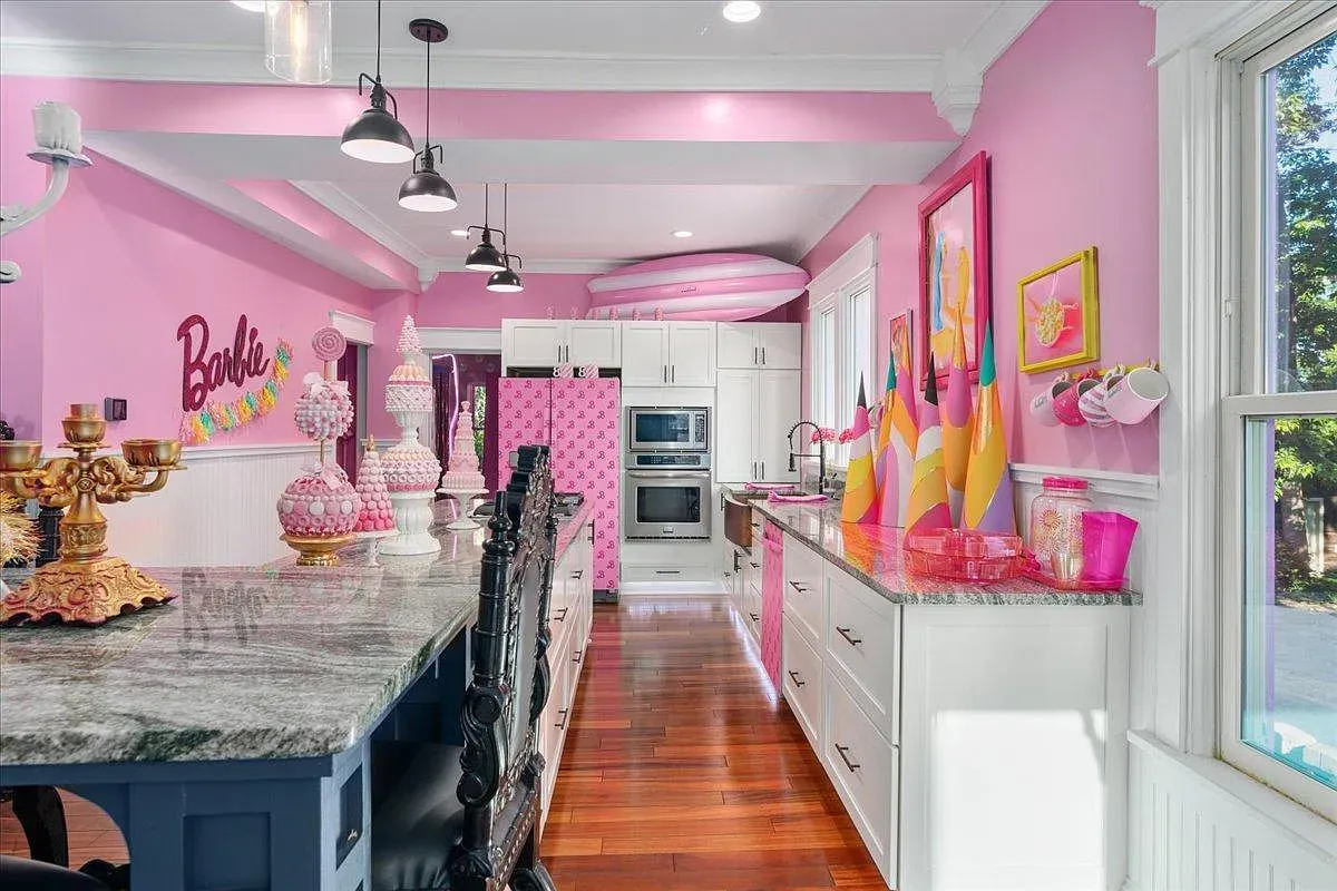 ## Kitchen runs bright Barbie-pink, with a feature wall of playful art; good counter space and a cheerful vibe for morning coffee.