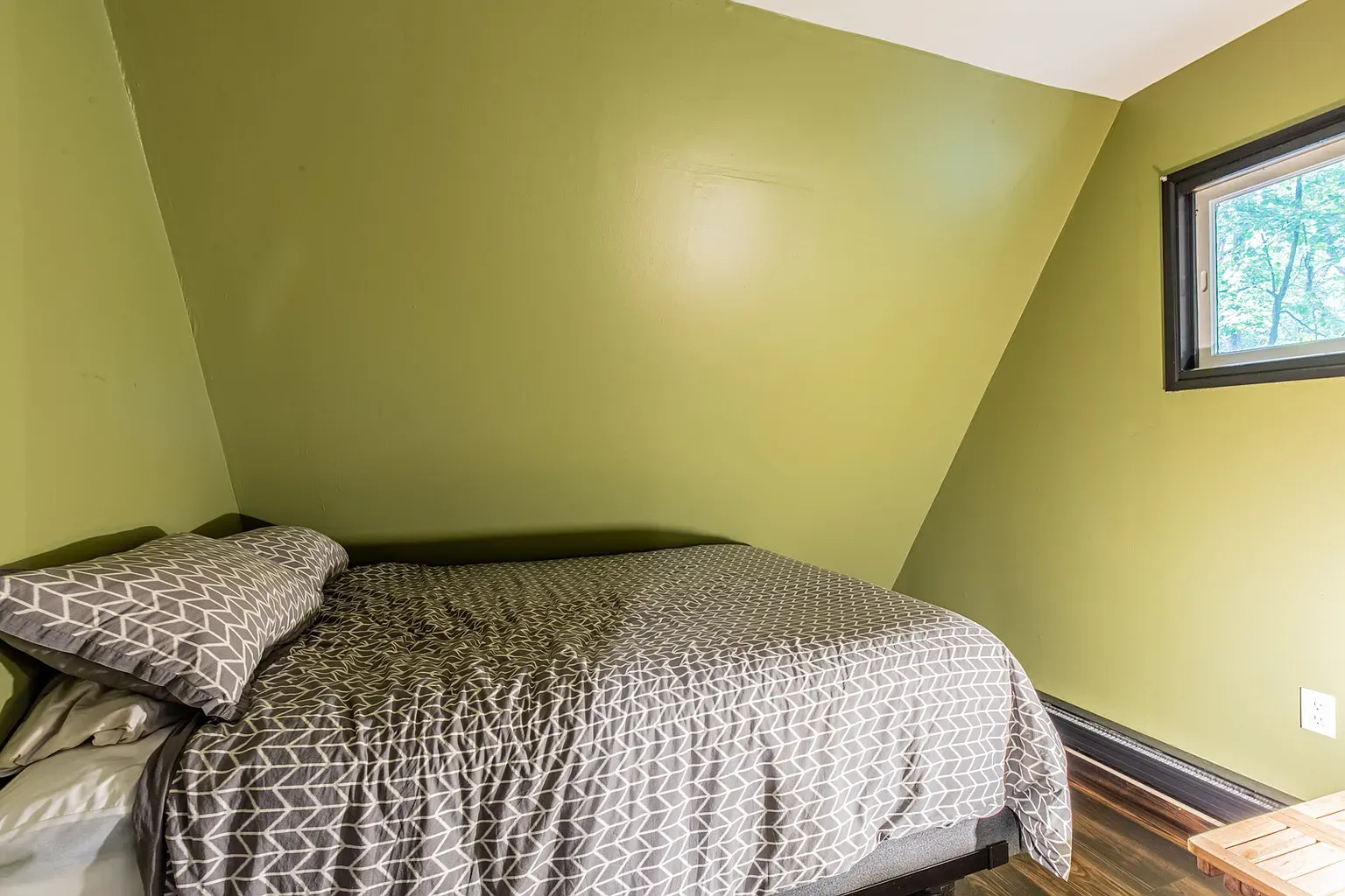 Bedroom hits with olive wall and slanted ceiling. Simple, calm.