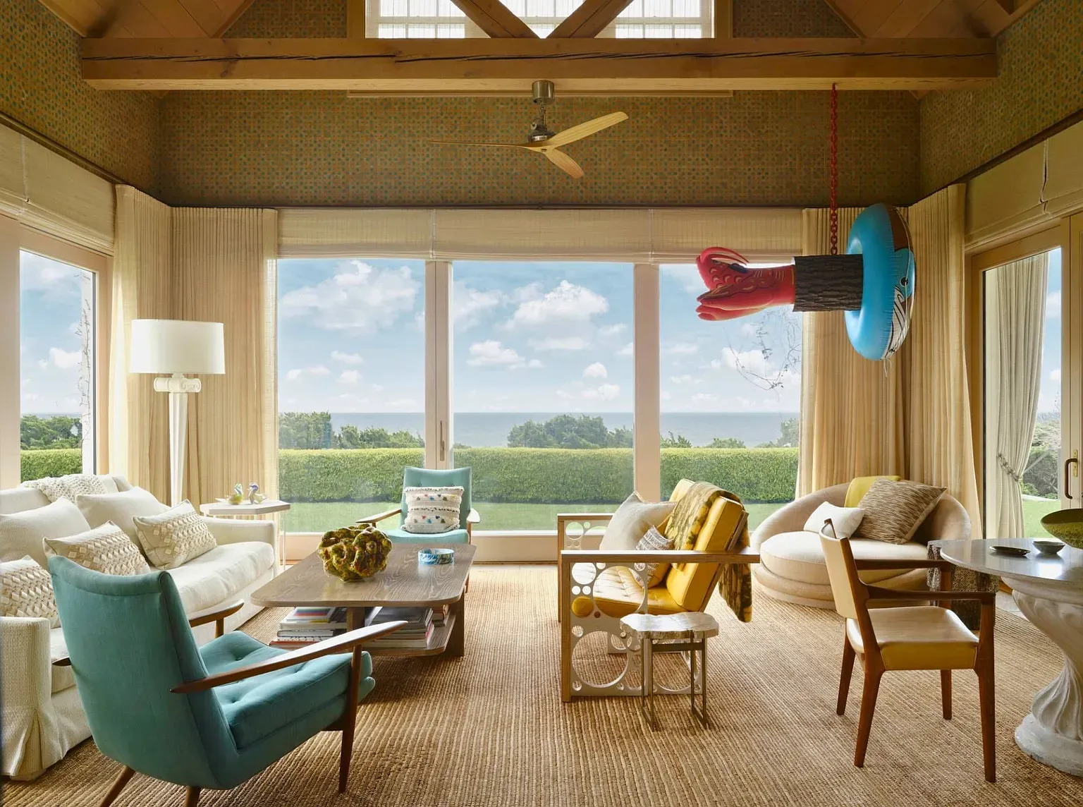 "You've got to see this living room! The big windows let in so much light and offer a great view of the greenery outside. I love how the furnishings mix bright colors with a relaxed vibe—check out that funky lobster sculpture! It’s such