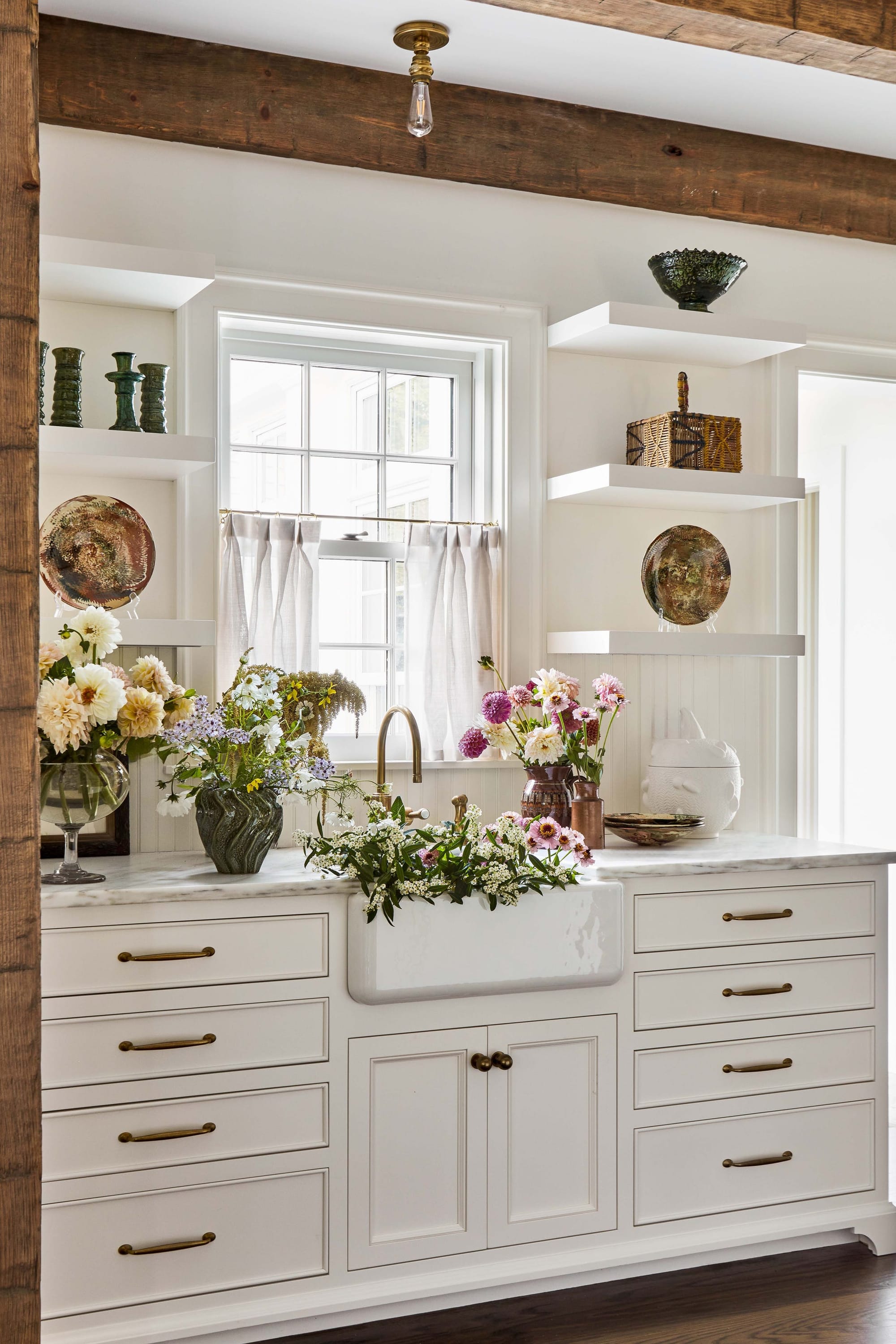 "Rustic Elegance Meets Farmhouse Charm in this Stunning White Kitchen with Exposed Beams and Fresh Flower-Filled Sink!"