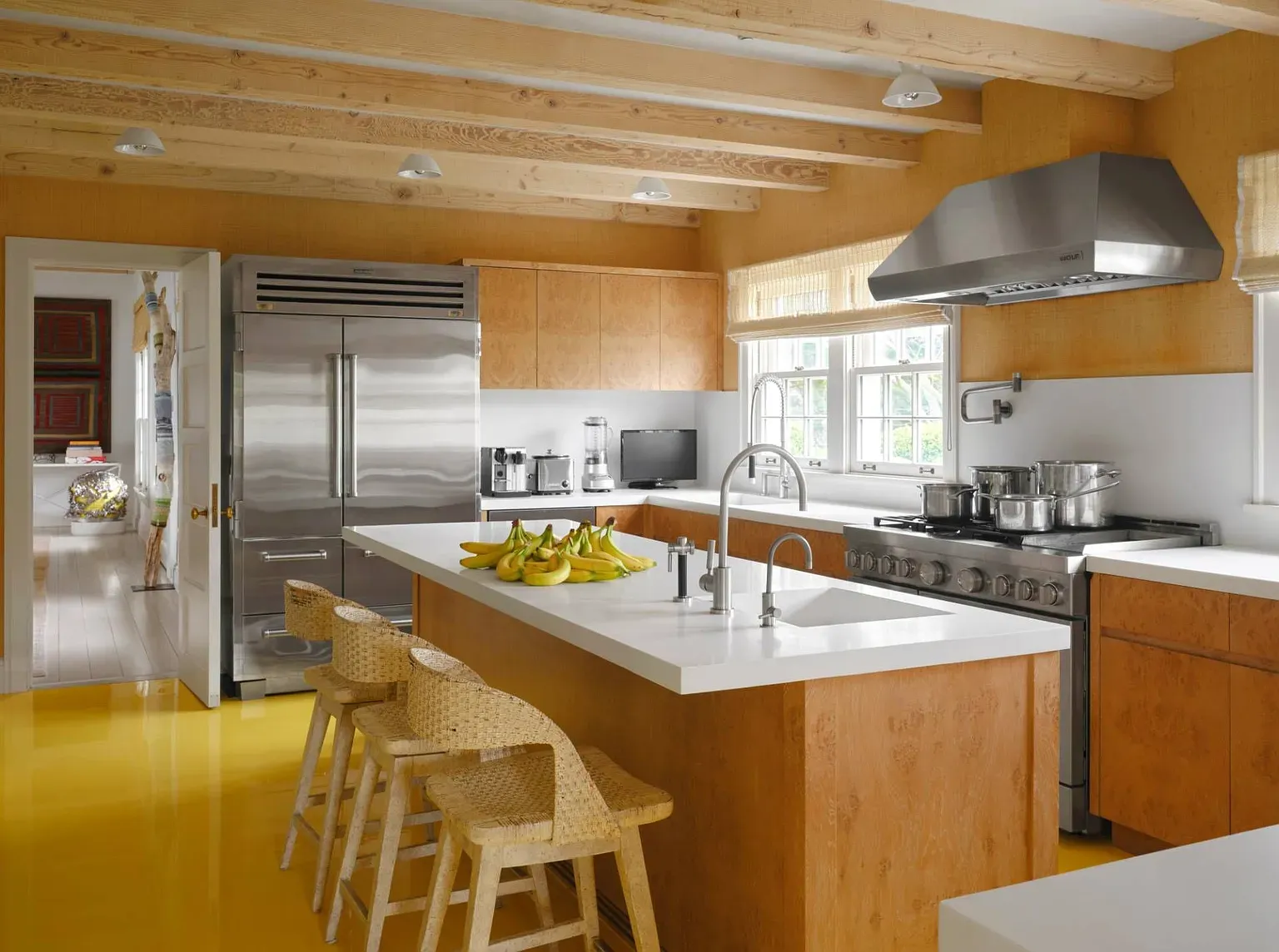 "Here’s the kitchen—it has a bright and cheerful vibe with those yellow floors! I love how the wooden beams add a warm touch, and there’s plenty of space to whip up a feast. Plus, check out that sleek stainless steel range;