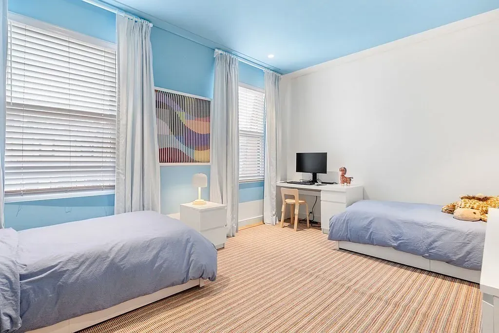 "Here’s a bright and cheerful bedroom that’s perfect for kids! It has two cozy beds, and I love how the blue ceiling makes it feel spacious. There’s a little desk for homework or crafts, and those curtains let in just the right