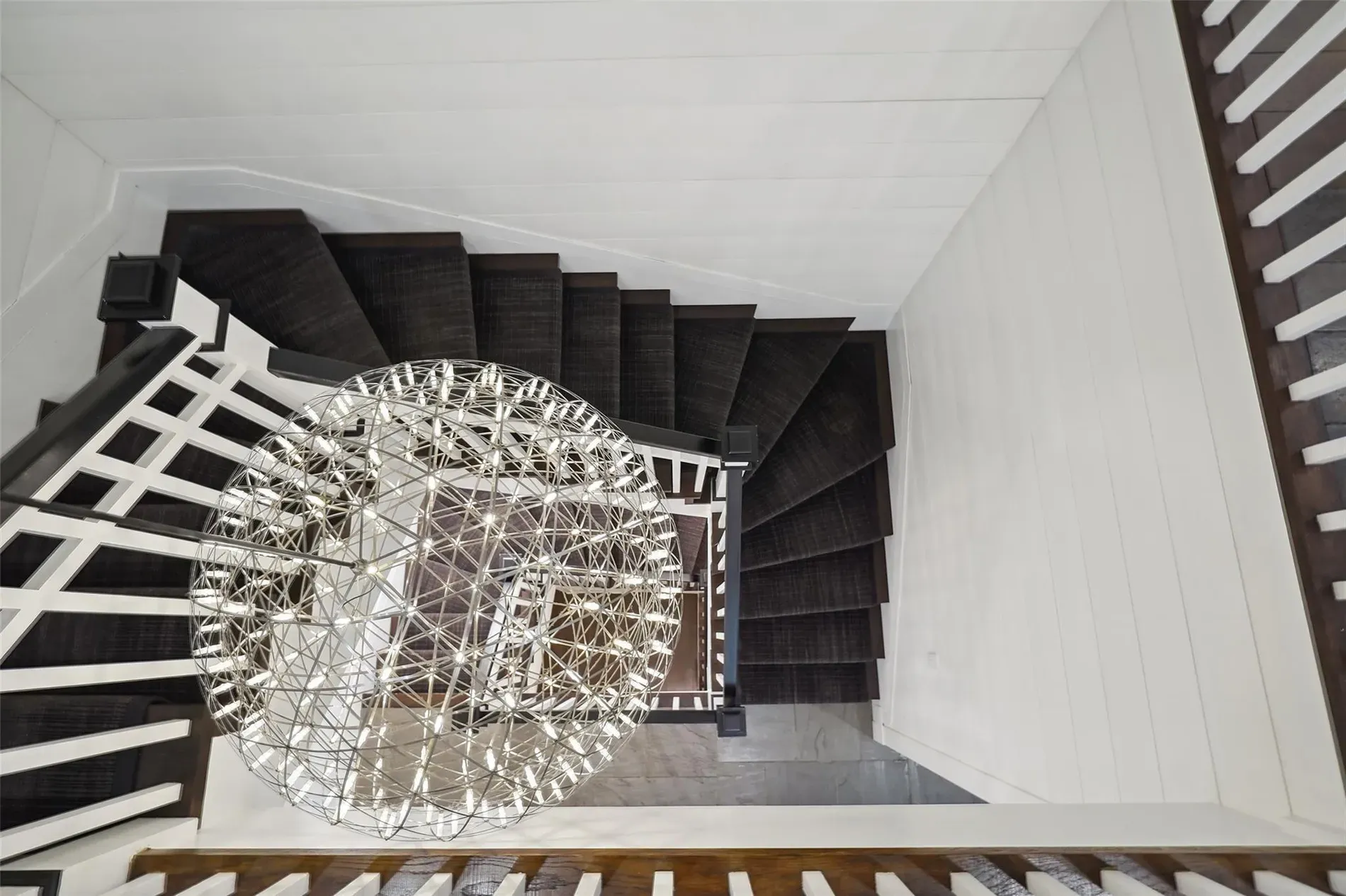 This staircase angle is doing it—dark steps, white rails, chandelier flex.