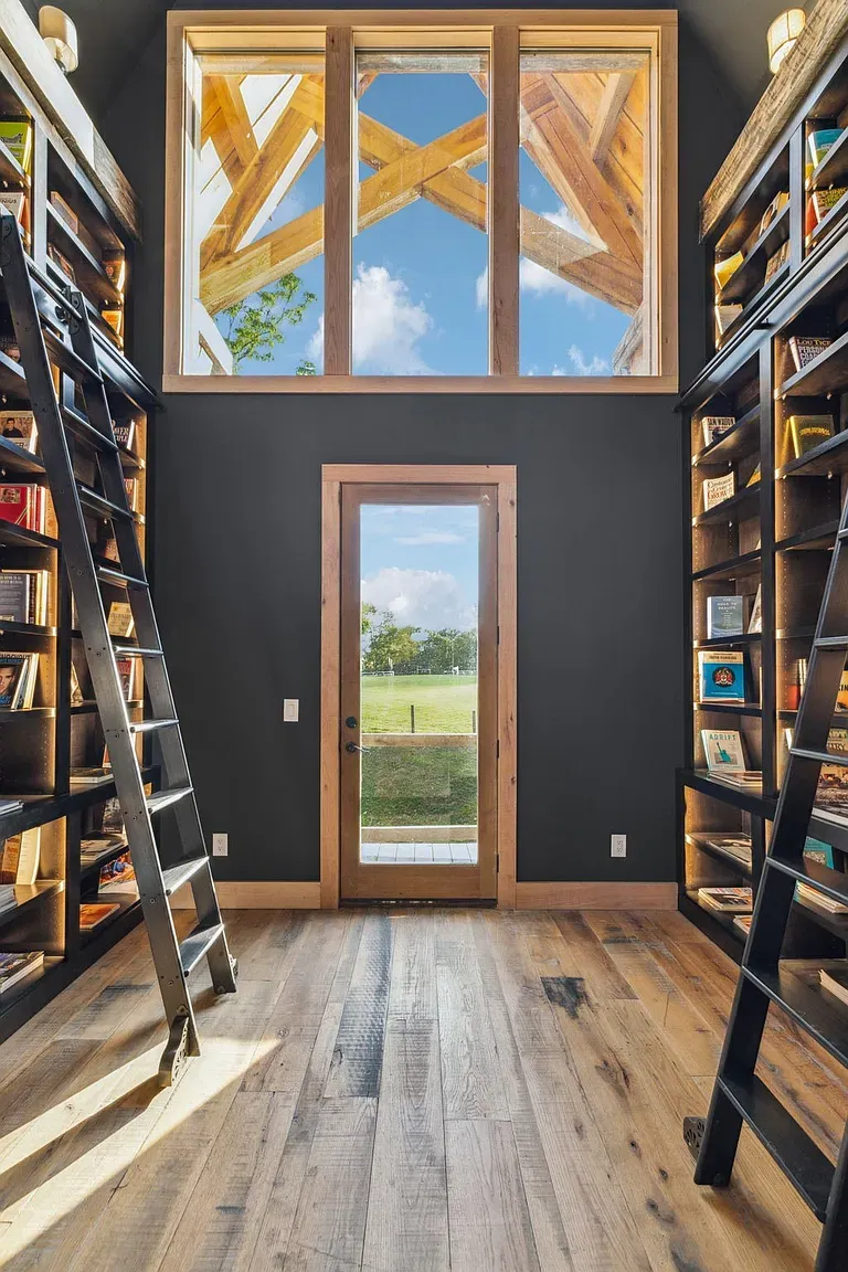Two-story library moment. Charcoal walls, soaring shelves, and a cozy perch up top.